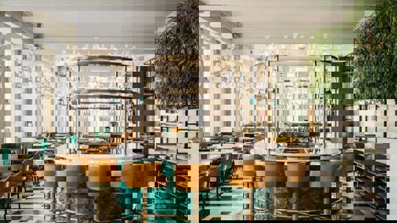 A refined bar with contemporary Scottish decor, navy-blue banquettes, soft overhead lighting, marble tabletops, and neatly arranged bottles behind the counter.