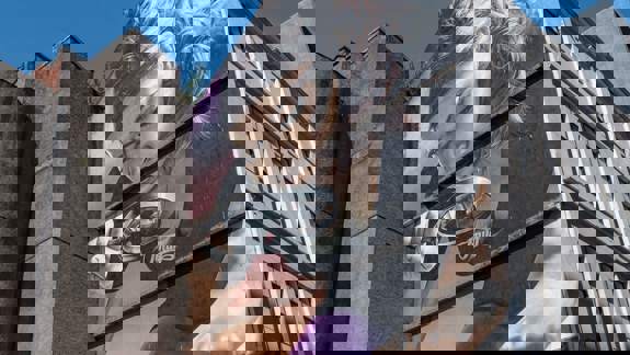 Mural of a woman looking through a magnifying glass, seemingly at the street below.