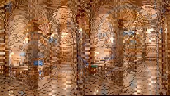 A view of the ornate interior of a building with arches and columns, a staircase, and patterned floor.