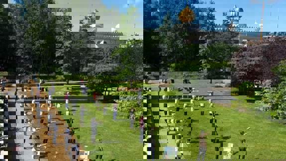 A group of people standing on a grassy lawn in a park, performing a group exercise activity on a sunny day.