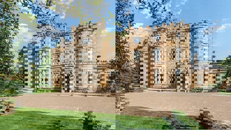 Grand exterior of Crossbasket Castle surrounded by manicured lawns and gardens, showcasing its historic stone architecture and turreted façade on a bright day.