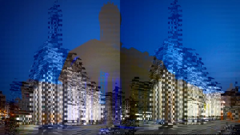 The Gallery of Modern Art (GOMA) at night, with its classical facade and columns dramatically lit against a dark blue sky.