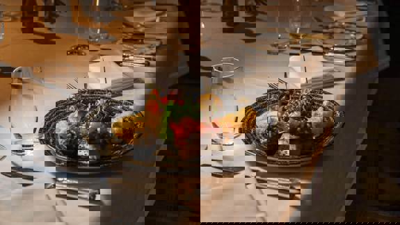 A plate of appetizers, including bruschetta and fried items, sits on a white tablecloth with cutlery, napkins, and empty wine glasses set around it.