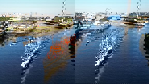 A classic-looking tour boat, the Waverley, travels along the River Clyde with people on its decks, with a modern city skyline in the background.