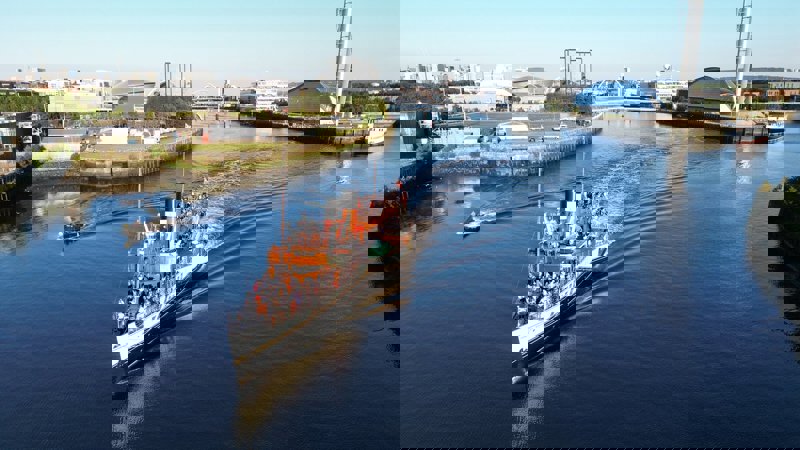 A classic-looking tour boat, the Waverley, travels along the River Clyde with people on its decks, with a modern city skyline in the background.