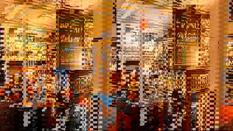 A crowded bar scene at The Pot Still pub, filled with rows of whisky bottles.