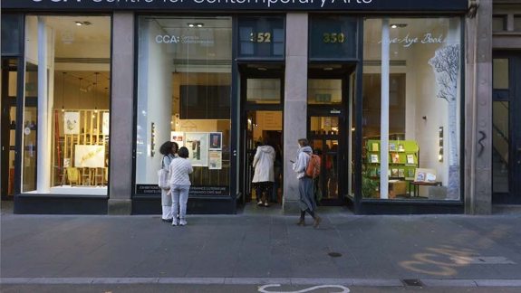 Storefront of the CCA: Centre for Contemporary Arts. Large glass windows display art pieces and books. People enter, creating a lively and inviting atmosphere.