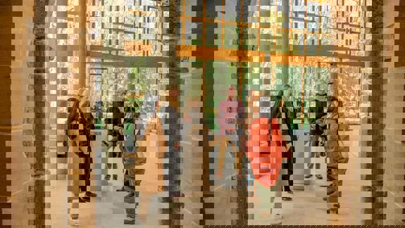 A small tour group gathers around an exhibit inside the museum, which has large windows and stone columns.