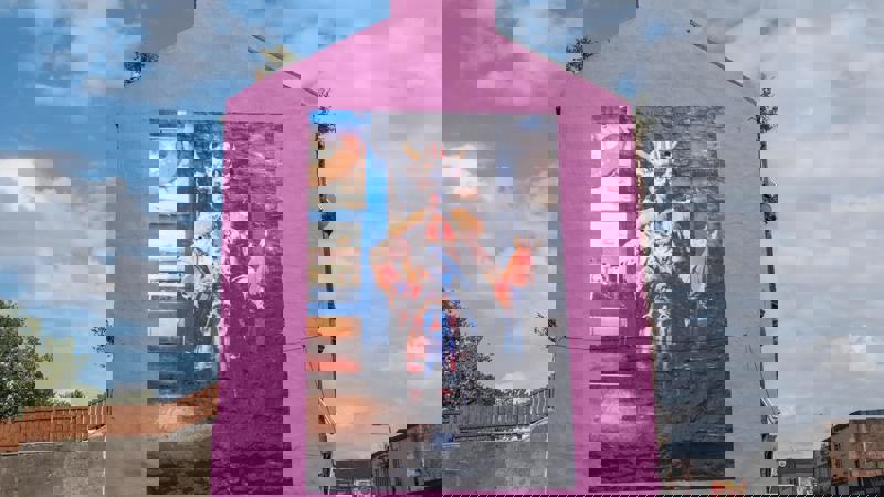 Bright pink building with a large mural of Billy Connolly in a fantastical, colourful costume with a horned helmet.