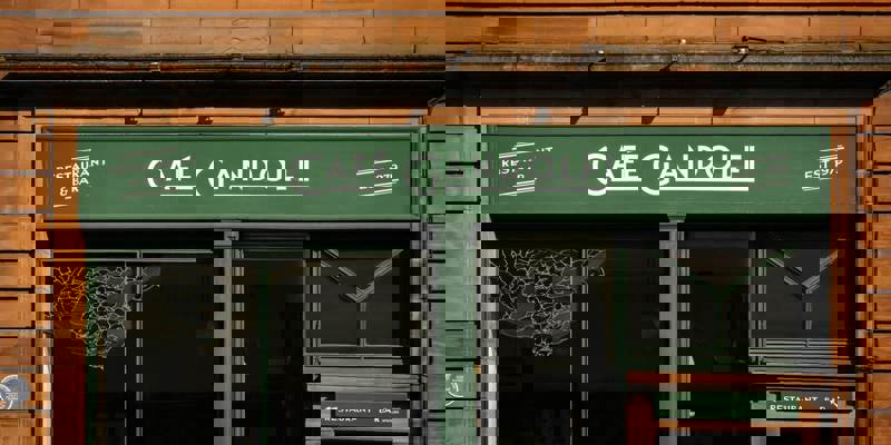 A restaurant and bar with a green sign reading "Café Gandolfi," set against a brown stone building.