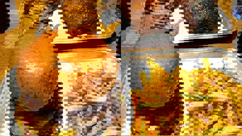 Two trays of food with burgers, fries, onion rings, and ribs.