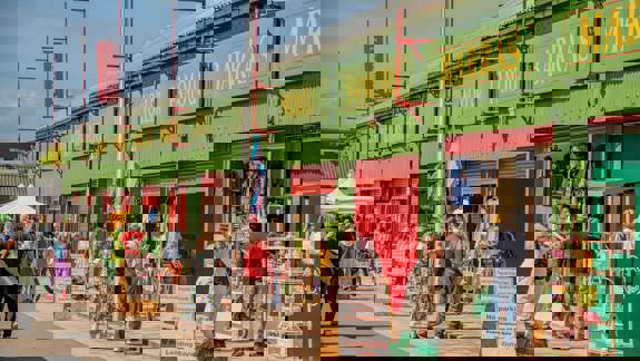 People browse goods at outdoor stalls with green and red storefronts at The Barras Market.