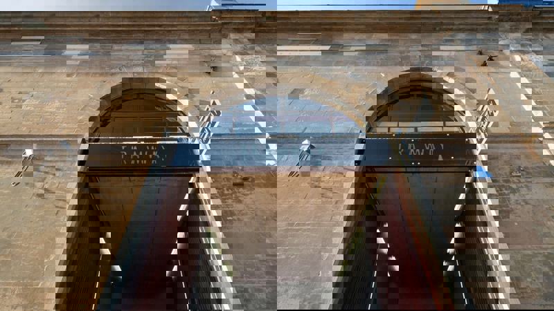 A low-angle shot of the entrance to the Tramway arts venue, featuring a large arched doorway and the building's stone facade.