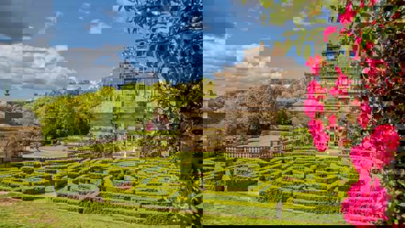 The manicured gardens of Pollok House, with a building in the background and bright pink flowers in the foreground.