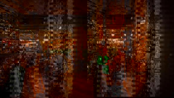 A couple sits at a candlelit table in a cozy, dimly lit bar with books and paintings on the walls.