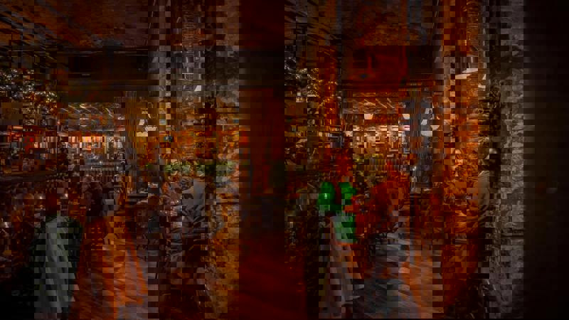 A couple sits at a candlelit table in a cozy, dimly lit bar with books and paintings on the walls.