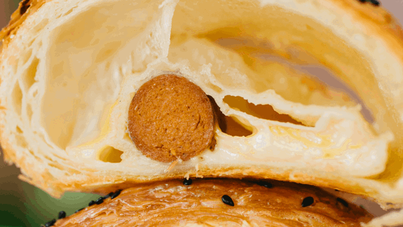 Golden-brown pastry with flaky crust, melted cheese filling, baked-in sausage, and black sesame seed topping.