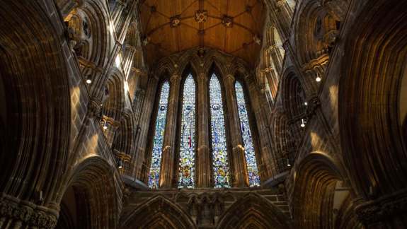 Interior of Glasgow Cathedral with tall stained glass windows and vaulted stone arches.