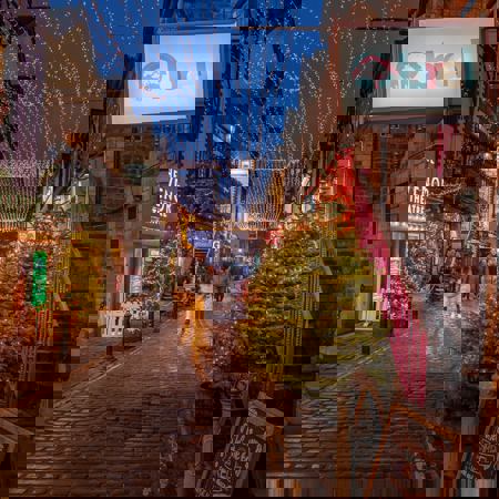 A cobblestone lane in Glasgow called Ashton Lane is decorated for Christmas with string lights overhead and illuminated trees outside The Grosvenor Picture Theatre and Brel bar.