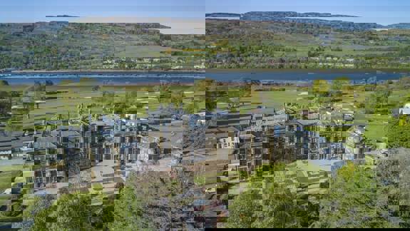 Aerial view of Mar Hall Golf and Spa Resort near Glasgow, showcasing the grand historic mansion, landscaped gardens, and River Clyde with scenic hills beyond.