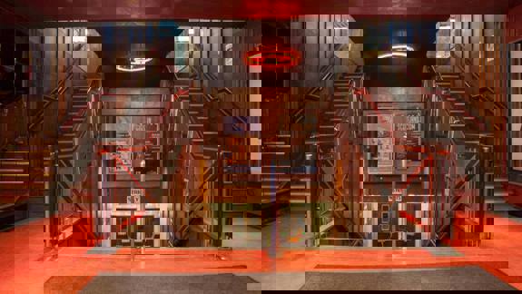 The main internal staircase of the Barrowland, featuring a symmetric design with red carpet flooring and dark wood paneling leading down into the foyer.