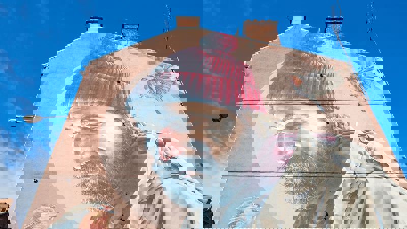 A large, detailed mural of a bearded man in a red hat with a robin on each side of him, painted on the side of a building.