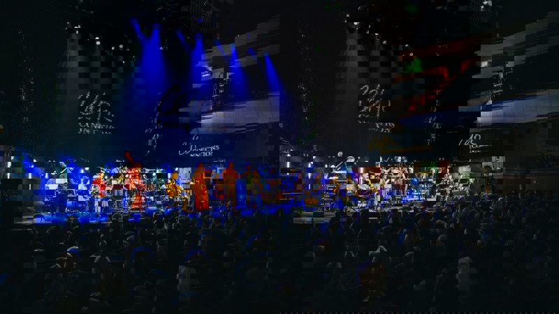 A band performs on a stage lit with spotlights to an audience at the Celtic Connections music festival.