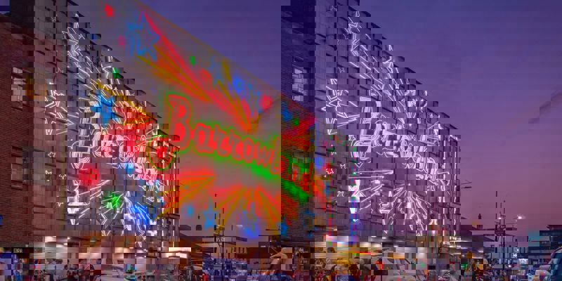 The iconic Barrowland Ballroom building at dusk, illuminated by vibrant neon stars and its name in lights.