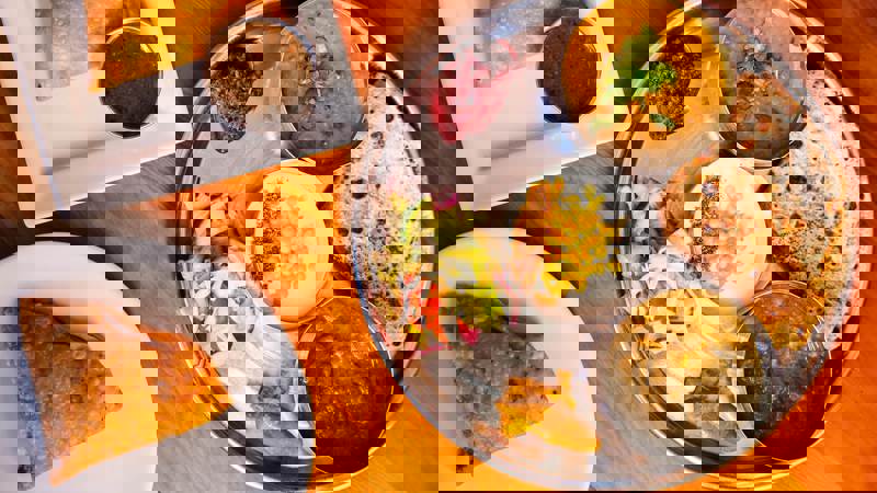 An overhead shot of two plates of Indian food, one with a thali platter and the other with a samosa.