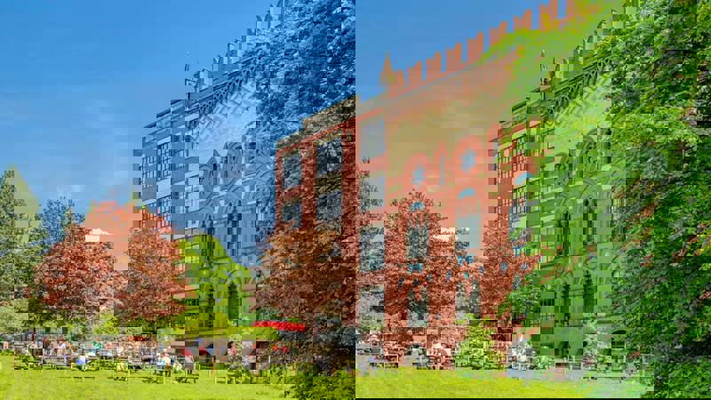 A view of a large, modern building with a grassy lawn and people sitting at tables outside.