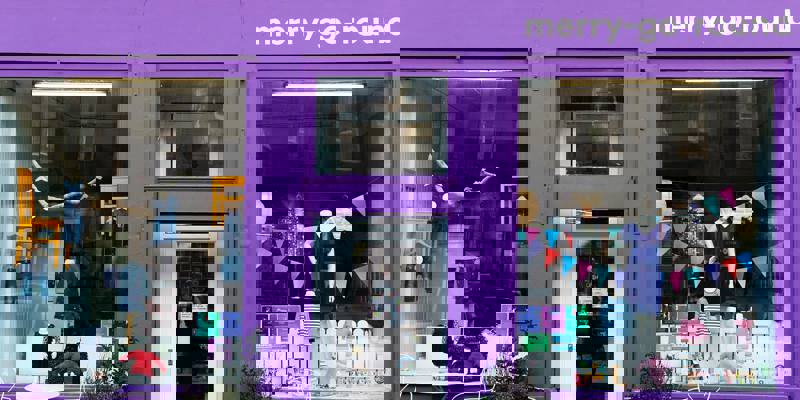 The storefront of merry-go-round, a children's clothing shop painted a vivid purple. Clothes are visible in the large window displays next to the main glass door.