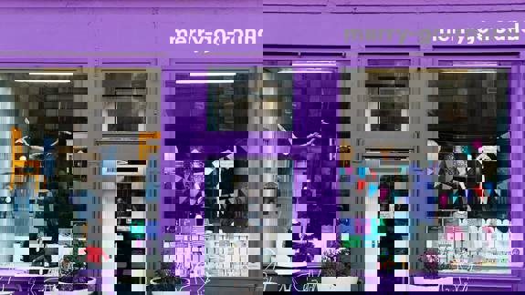 The storefront of merry-go-round, a children's clothing shop painted a vivid purple. Clothes are visible in the large window displays next to the main glass door.