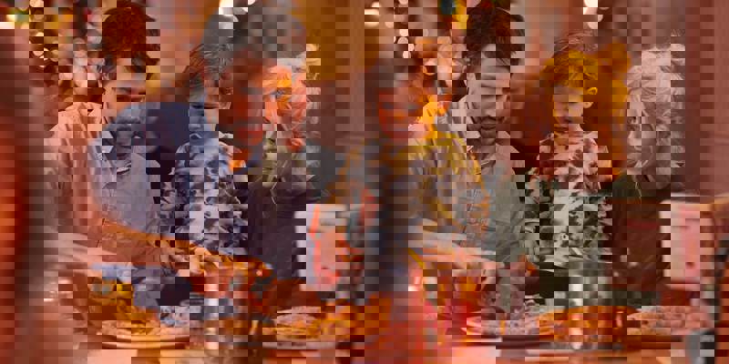 Family seated at a restaurant table, with one adult serving food and another holding a child.