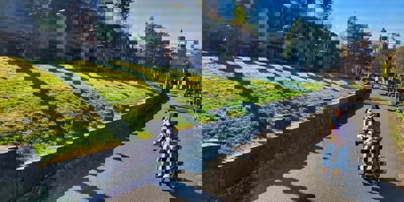 A person in a wheelchair on a paved path in the Glasgow Necropolis, surrounded by gravestones and green hills.