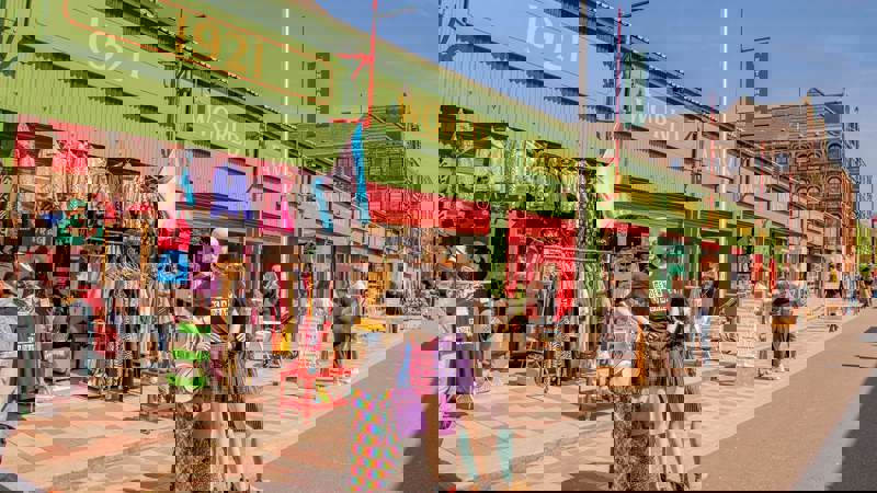 A street view of a market with mannequins and clothing racks outside a row of green and red shops.