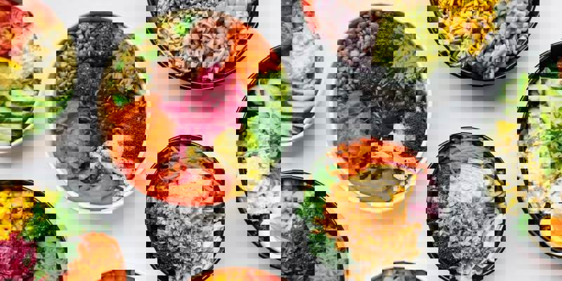 An overhead shot of three plant-based wraps filled with colorful fresh vegetables and green garnish, served on a plate.