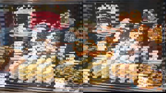 A bakery display case filled with sliced red velvet cake, brownies, cookies, mini bundt cakes, and layered sponge cakes.