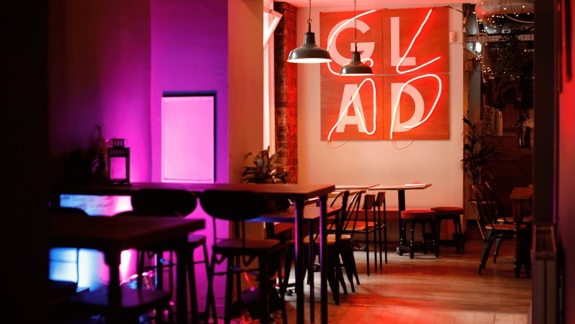 Interior of a café with neon "GLAD" sign and purple-red ambient lighting.
