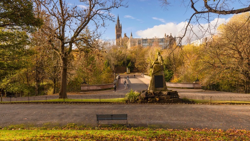 A beautiful park scene in autumn with a path, trees, and a distant building with a spire under a blue sky.