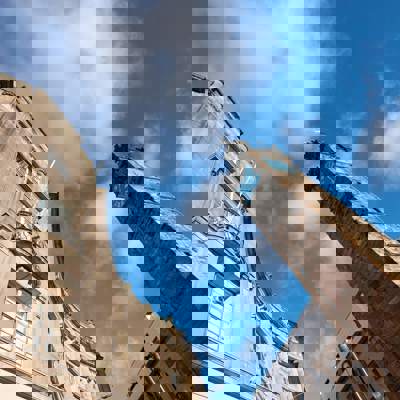 A low-angle view of the historic Tolbooth Steeple and an adjacent building against a bright blue sky with clouds.
