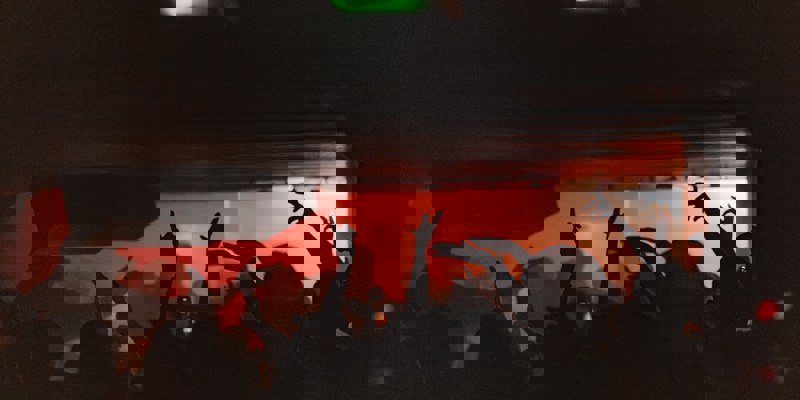 Silhouettes of club-goers with raised arms dancing in the Sub Club, lit by red stage lights and low ceilings.