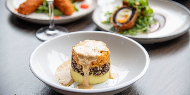 A close-up shot of a plate of haggis, neeps, and tatties at Mharsanta, a Scottish restaurant, with other dishes blurred in the background.