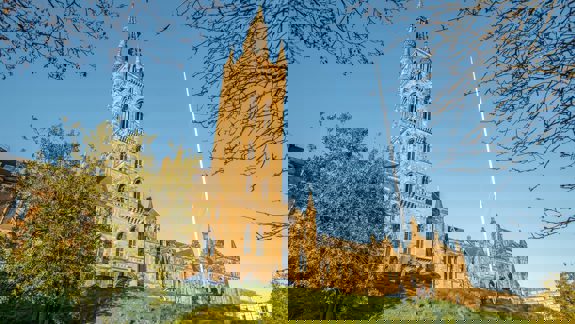 A beautiful view of the University of Glasgow's main building, a striking gothic-style tower with a tall spire, on a sunny day.