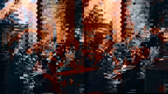 A group of five musicians playing instruments like the fiddle and cello in a dimly lit, rustic pub.