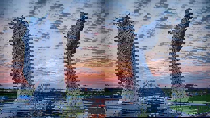 Two massive, sculptural horse heads made of steel rise from the water at sunset in Scotland.