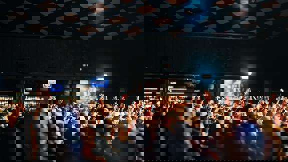 An energetic crowd inside the Barrowland Ballroom with many hands raised in the air, captured from the back of the venue looking toward the stage.