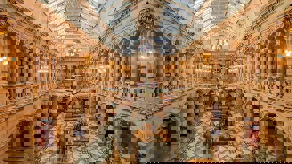 The grand, vaulted interior of a museum with a plane suspended from the ceiling and taxidermy animals, including an elephant and a giraffe, on the floor.