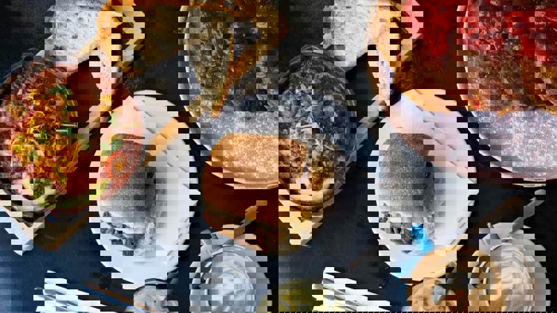 An overhead shot of a table with a skillet of shakshuka, a roll, French toast with strawberries, and two coffee drinks.