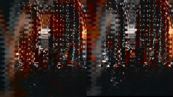 Audience watching a candlelit string quartet performance inside Òran Mór, with fairy lights and arched stone architecture.