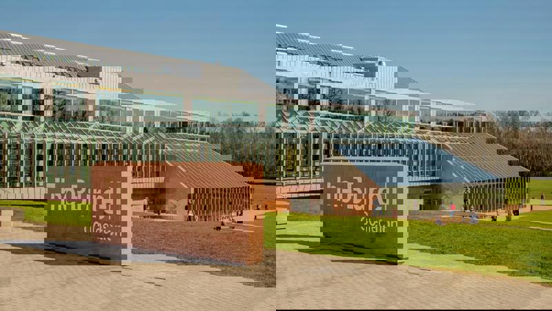 A modern museum building with large glass windows and a prominent stone sign that reads "The Burrell Collection" in front of a grassy lawn.